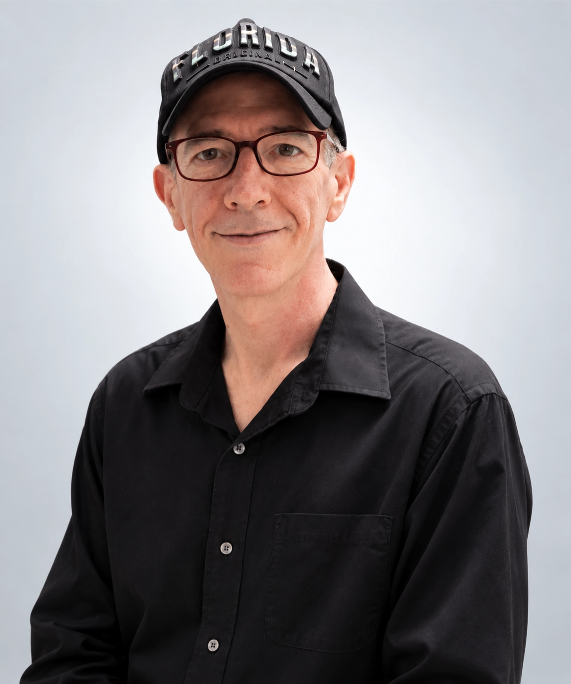 Scott Price wearing glasses, a black Florida cap and a black collared shirt against a soft gray background
